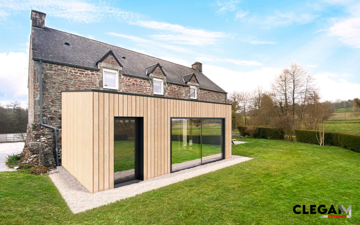 Maison en pierre de pays avec une extension en bois. Sur la façade, une porte vitrée et une grande baie vitrée double.